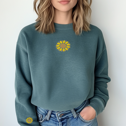 A woman wearing a green sweatshirt with embroidered sunflower motifs on the chest and wrist area, paired with blue jeans.
