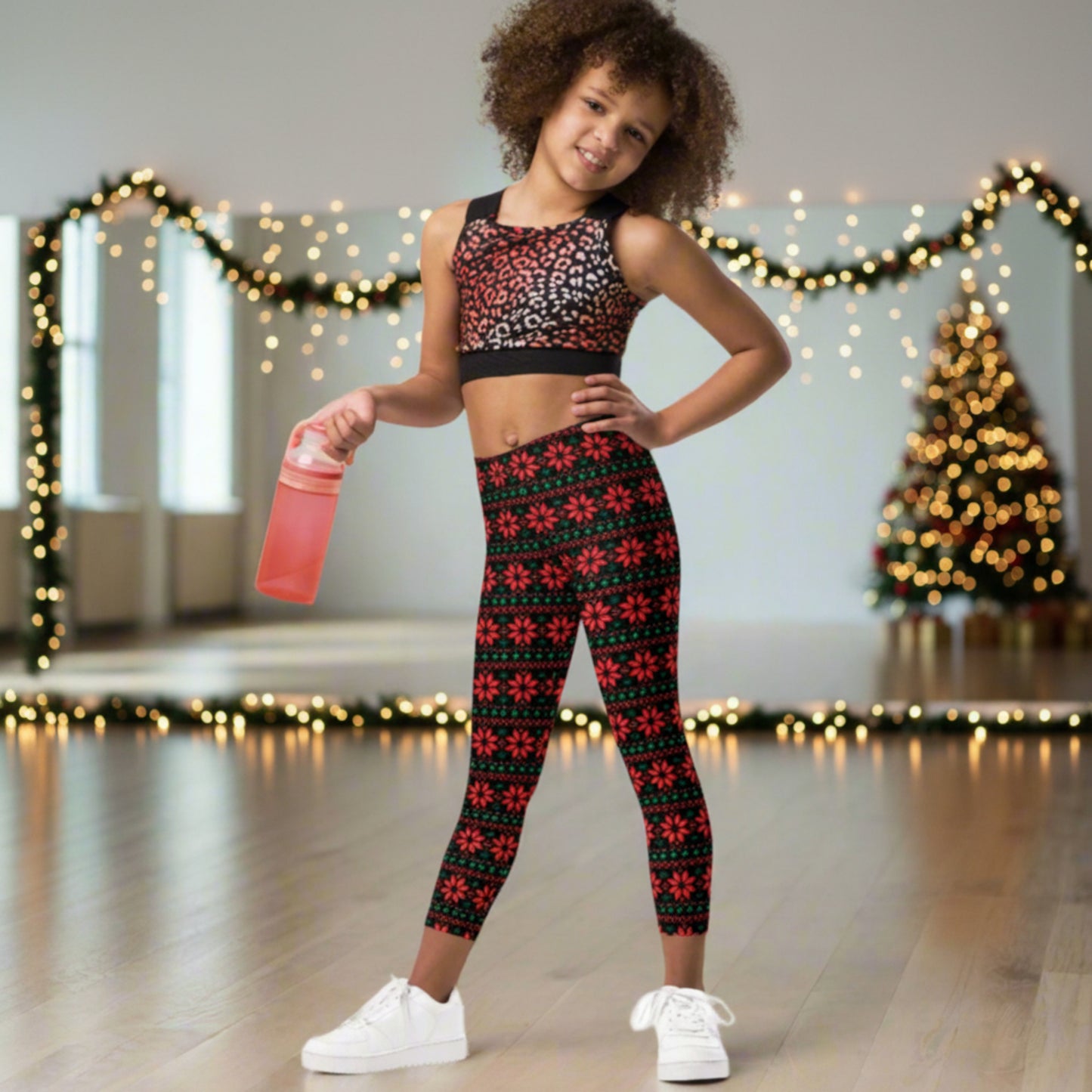 Festive holiday leggings for girls with vibrant red poinsettias and green leaves arranged in a repeating Fair Isle style pattern against a black background. These full length, high rise leggings are available in girls’ sizes 2T–20 for Christmas celebrations and winter outfits.