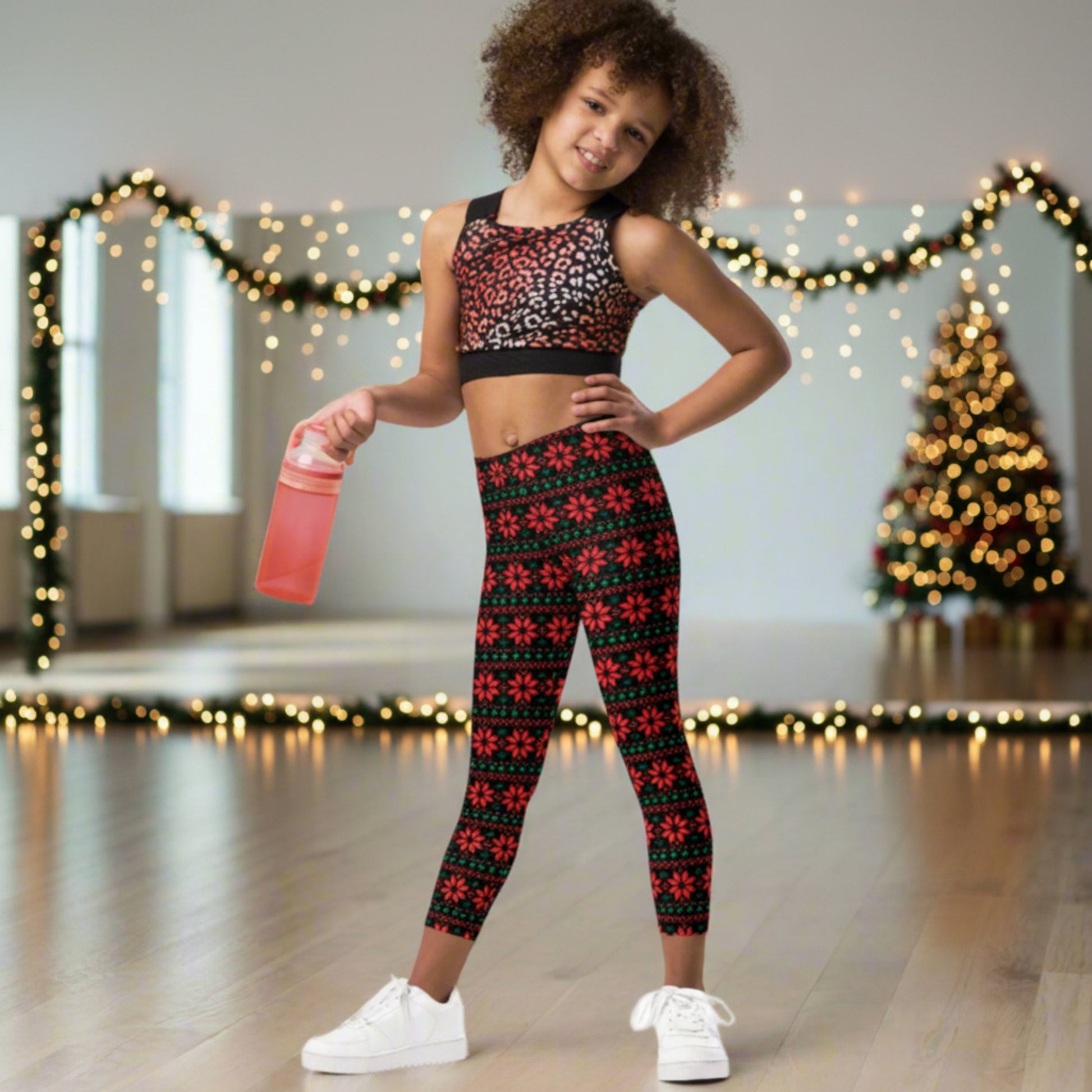 Festive holiday leggings for girls with vibrant red poinsettias and green leaves arranged in a repeating Fair Isle style pattern against a black background. These full length, high rise leggings are available in girls’ sizes 2T–20 for Christmas celebrations and winter outfits.