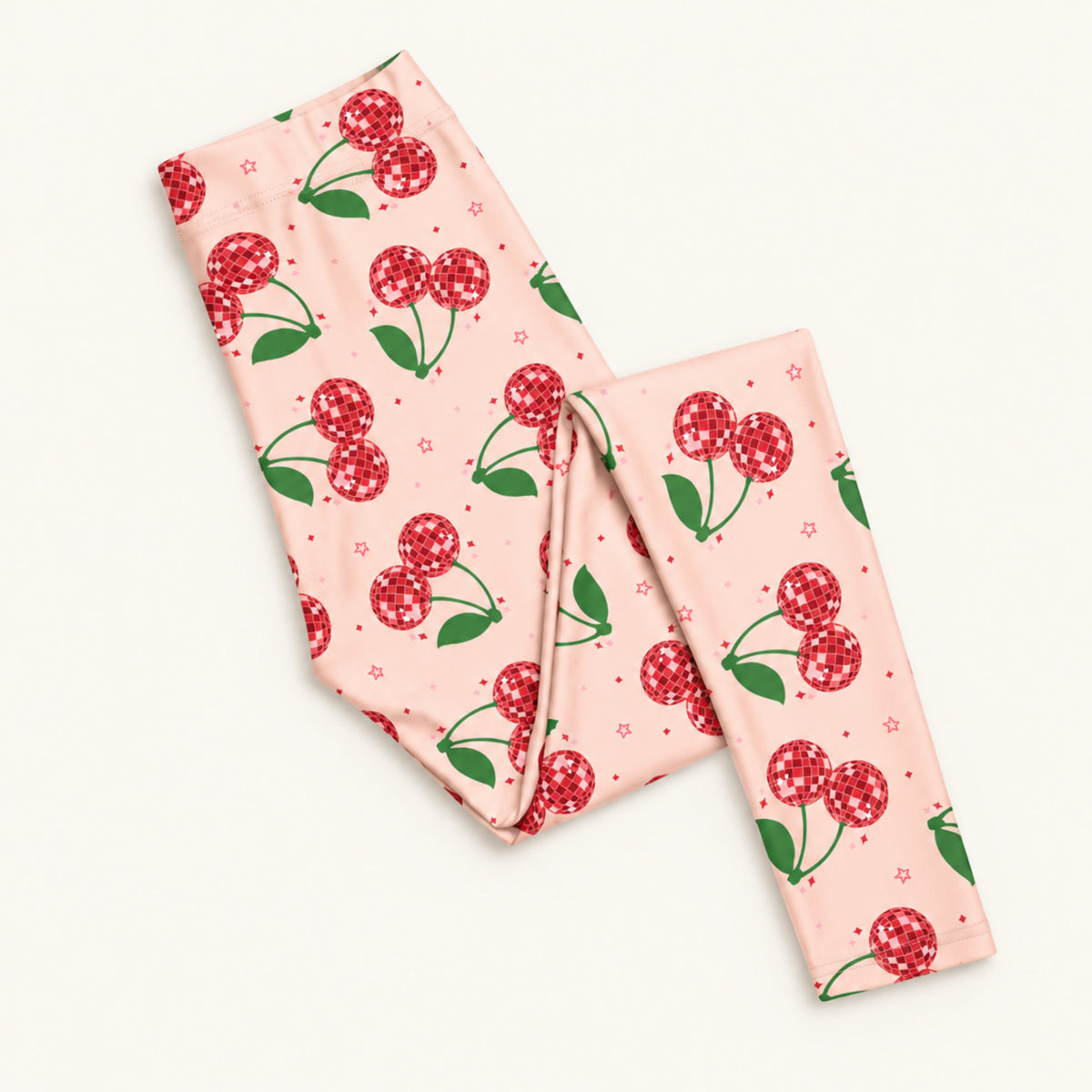 Folded pink cherry print womens leggings showing the bright pink fabric, sparkling red cherry design and comfortable mid rise waistband. The full length leggings feature a playful retro fruit print with a colorful Cherry Girl feel, making them a fun choice for cute, feminine and nostalgic everyday fashion.