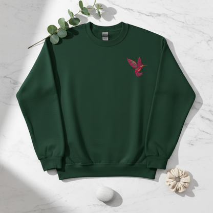 Forest green Gildan crewneck sweatshirt featuring a colorful embroidered hummingbird on the upper chest. The deep green background complements the natural bird design and gives the sweatshirt a cozy outdoors inspired feel. This color works especially well for casual fall and winter outfits while remaining easy to wear throughout the year. A fun choice for hummingbird lovers, gardeners, bird watchers, and nature enthusiasts.