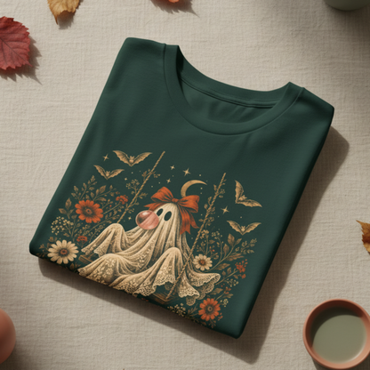 Forest green girls Halloween T shirt shown folded with a vintage inspired ghost blowing a bubble with bubble gum, surrounded by orange flowers, botanical foliage, bats, stars, lace and a bow. A cute spooky season graphic tee for girls who love vintage Halloween and fall fashion.