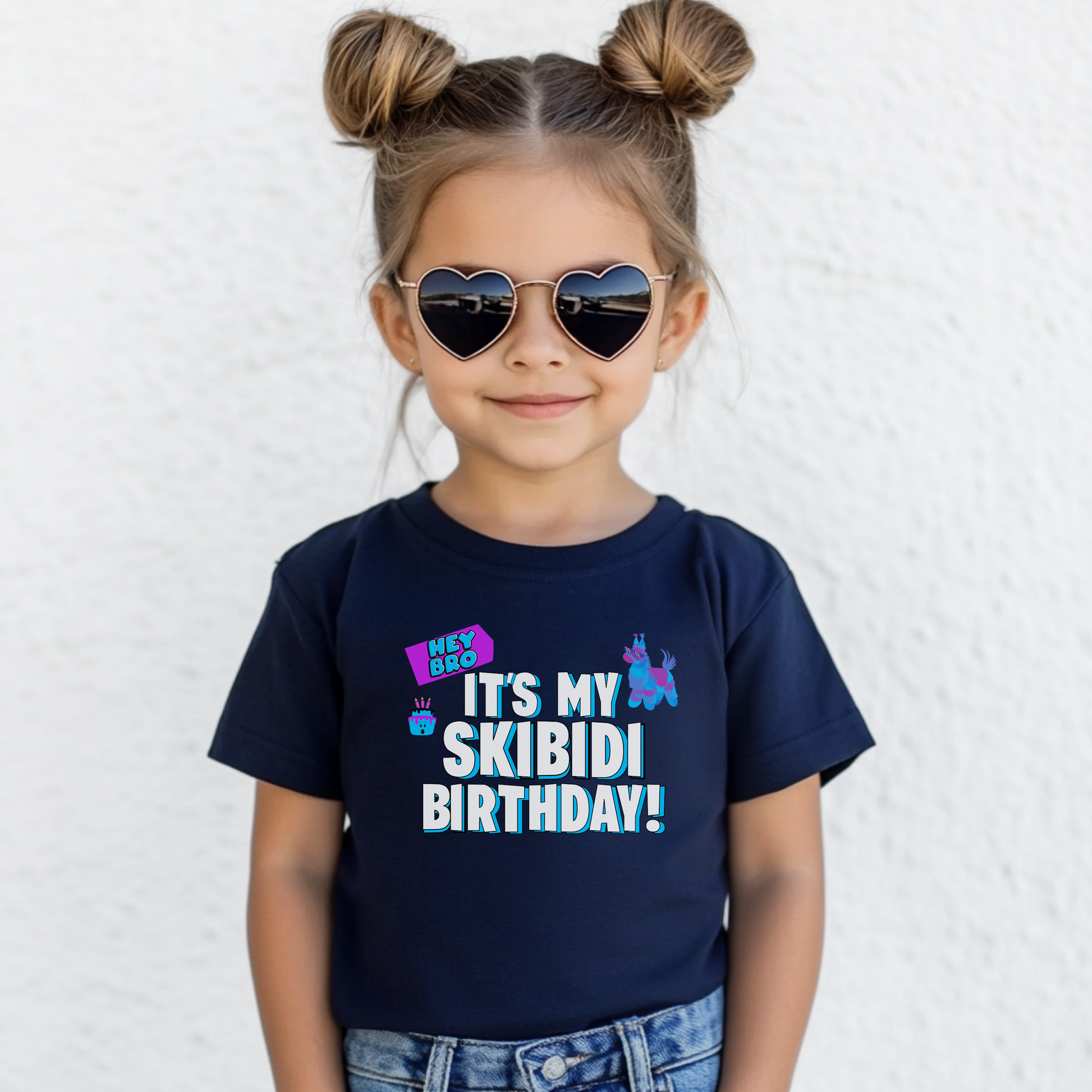 A young girl with her hair in two buns and heart-shaped sunglasses is wearing a navy blue t-shirt with a colorful graphic that reads 'IT'S MY SKIBIDI BIRTHDAY!' in white, blue, and pink text. She is standing against a white textured wall. Funny Skibidi birthday shirt for kids featuring bold blue and white It’s My Skibidi Birthday lettering with colorful birthday graphics, shown on a black youth t shirt for a fun Gen Alpha birthday outfit  