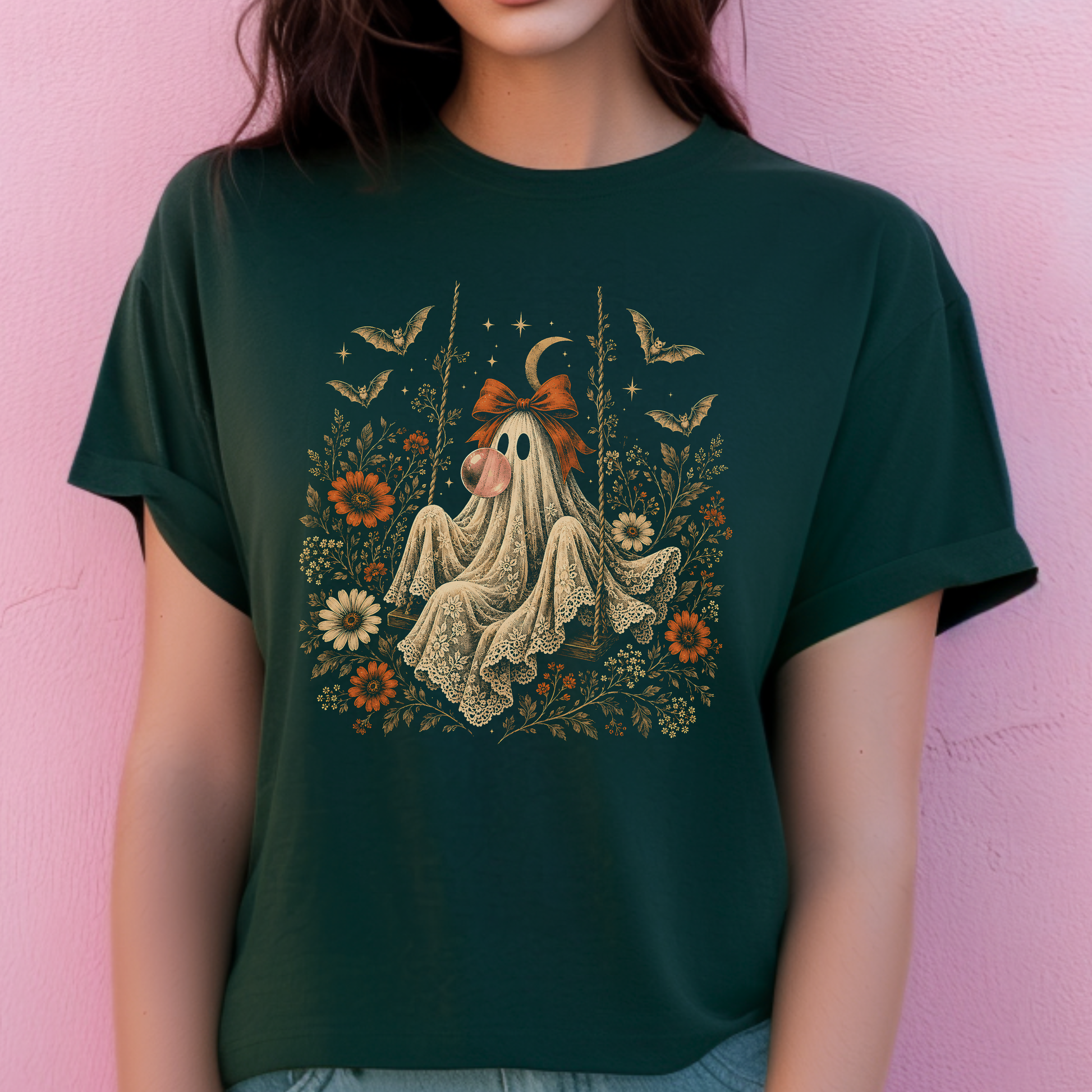 Vintage ghost Halloween t shirt showing a ghost relaxing on a swing while blowing a bubble with bubble gum. Surrounding flowers, leaves, bats, lace details, stars and a crescent moon create a whimsical vintage inspired design for autumn.