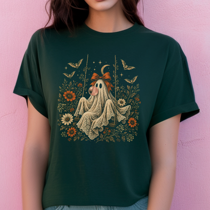 Vintage ghost Halloween t shirt showing a ghost relaxing on a swing while blowing a bubble with bubble gum. Surrounding flowers, leaves, bats, lace details, stars and a crescent moon create a whimsical vintage inspired design for autumn.
