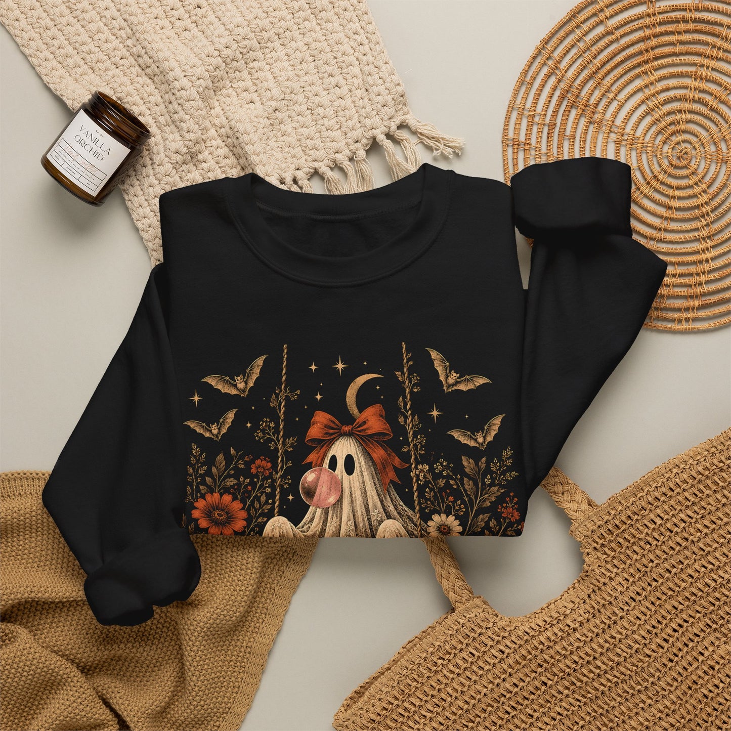 Vintage ghost on swing Halloween sweatshirt featuring a bubble gum blowing ghost surrounded by detailed flowers, leaves, bats, lace, stars and a crescent moon. This whimsical graphic combines vintage Halloween style with a romantic gothic and botanical aesthetic for fall.