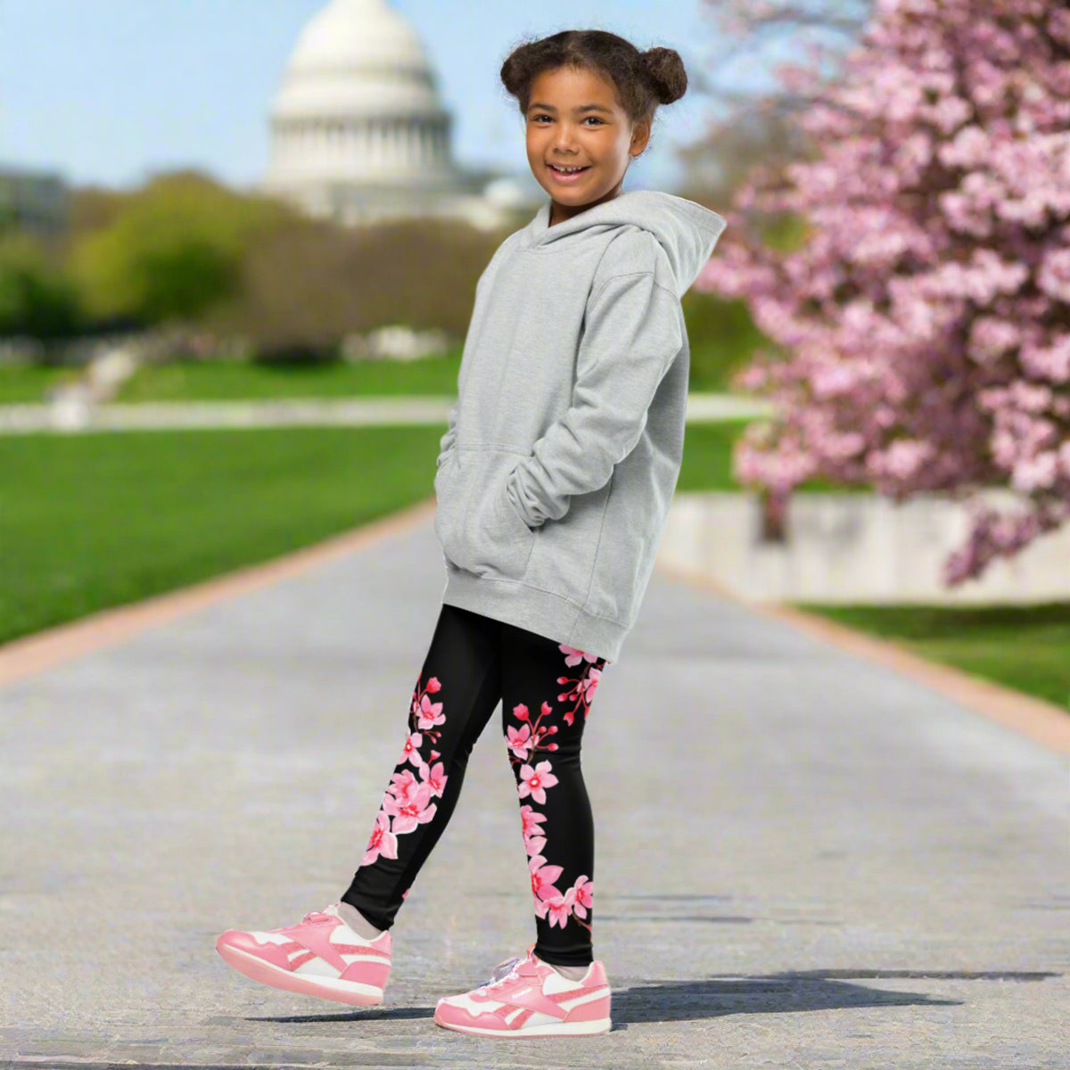 Young girl wearing black full length leggings with a delicate pink Japanese cherry blossom pattern while walking along a sidewalk in Washington DC. The high rise girls leggings combine a soft stretchy feel with a feminine sakura floral design, making them a comfortable choice for spring outings, sightseeing, family trips, cherry blossom season, school days, and everyday adventures.
