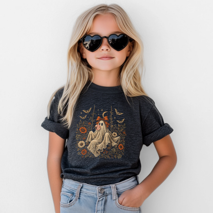 Girl wearing a dark heather grey Halloween T shirt featuring a whimsical ghost blowing bubble gum, surrounded by orange flowers, botanical foliage, bats, stars, lace and a bow. A vintage inspired girls graphic tee for spooky season, Halloween parties, fall activities and everyday autumn outfits.
