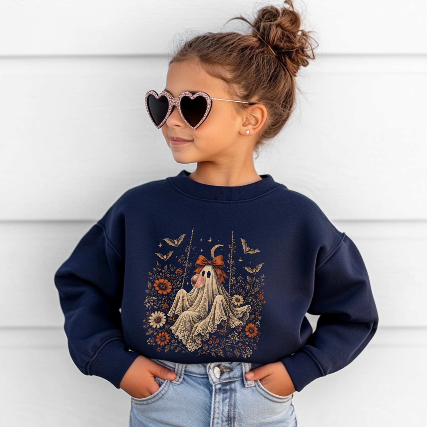 Girl wearing a navy Halloween sweatshirt with a vintage ghost blowing a bubble with bubble gum, surrounded by detailed flowers, botanical foliage, bats, stars, lace and a bow. A whimsical spooky season sweatshirt for girls, perfect for Halloween parties, pumpkin patches and fall outfits.