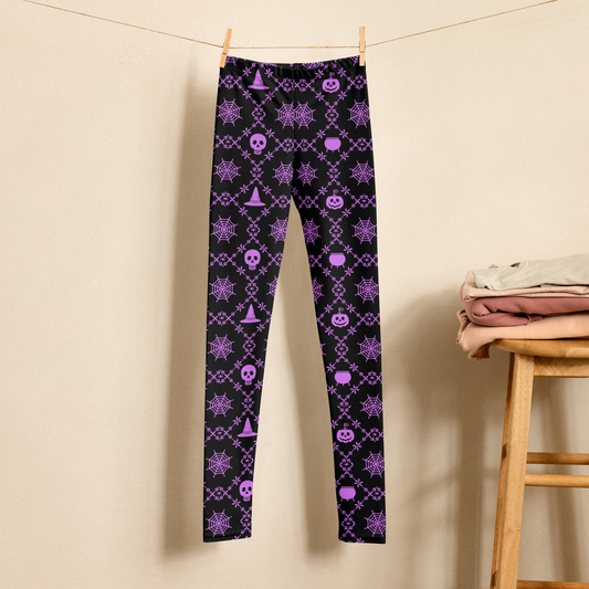 Girls gothic Halloween leggings featuring purple spider webs, skulls, witch hats, pumpkins, cauldrons, and decorative spooky patterns on a black background. The high waist, full length leggings are shown hanging in a neutral setting and are available in sizes 2T through 20 for toddlers, tweens, and teens. Matching women’s sizes are also available for Mommy and Me outfits.
