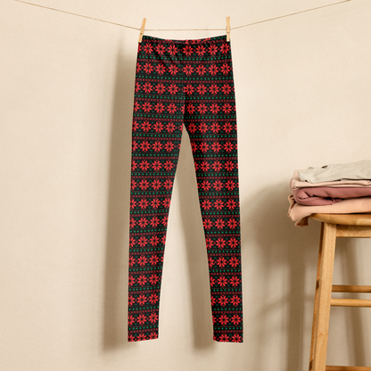 Girls Christmas leggings featuring a traditional fair isle pattern with red snowflakes and green accents on a black background. The high waist, full length leggings are shown hanging in a neutral setting and are available in sizes 2T through 20 for toddlers, tweens, and teens. Matching women’s sizes are also available for coordinated Mommy and Me Christmas outfits.