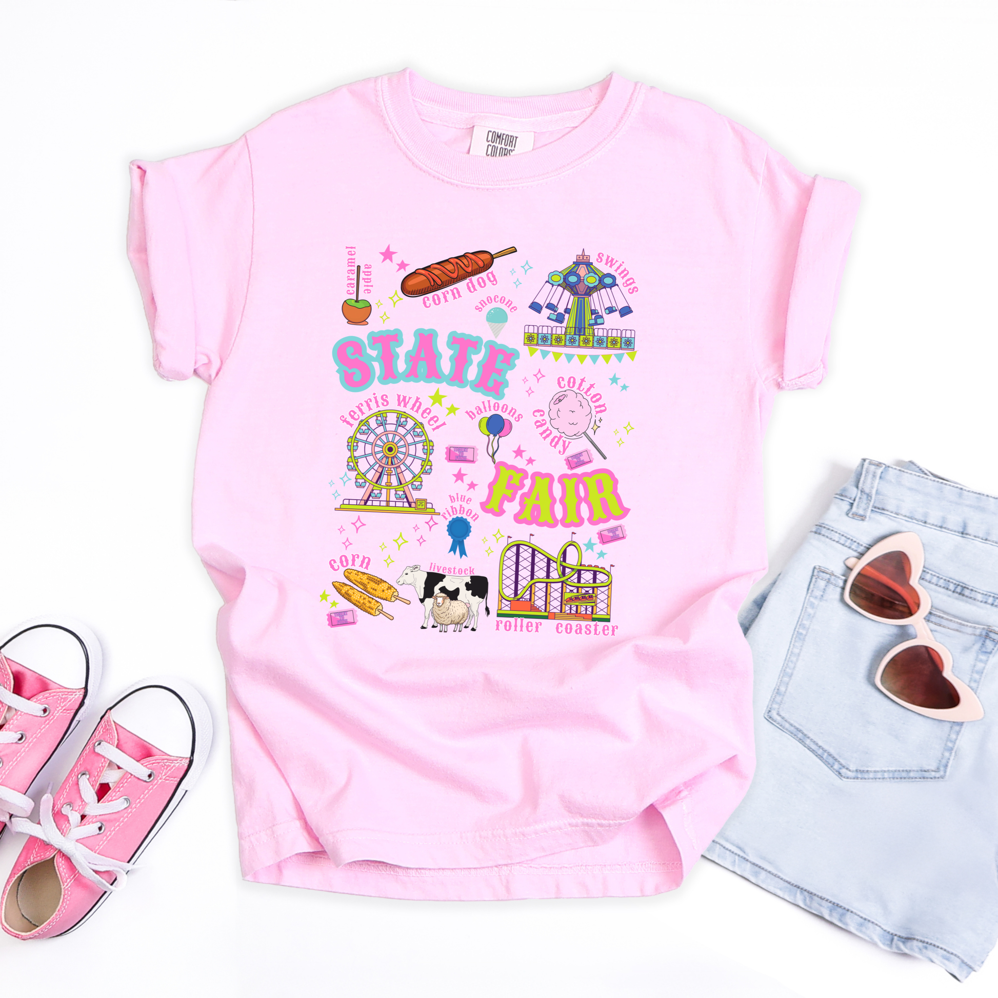Kids retro carnival T shirt featuring a colorful fair themed graphic with bold STATE FAIR lettering surrounded by a Ferris wheel, roller coaster, carnival swing ride, cotton candy, funnel cake, corn dogs, balloons, livestock, blue ribbon and colorful fair tickets. Perfect for a nostalgic summer fair outfit.