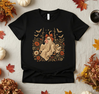 Black girls Halloween T shirt shown in a flatlay featuring a vintage inspired ghost blowing a bubble with bubble gum. The detailed graphic includes orange flowers, botanical foliage, bats, stars, lace and a bow, creating a cute spooky season shirt for girls who love unique vintage Halloween designs.