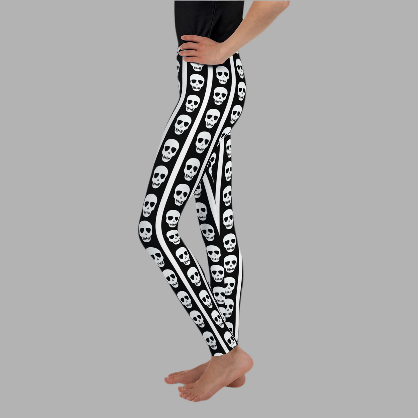Girls and tween skull leggings with bold black background and white vertical stripes accented by repeating skull graphics. Comfortable stretchy youth leggings designed for all day wear in sizes 8 to 20. Perfect Halloween leggings for tweens, school outfits, fall festivals, and spooky season styling. Soft breathable fabric ideal for active kids who love edgy gothic inspired fashion and standout statement pieces.