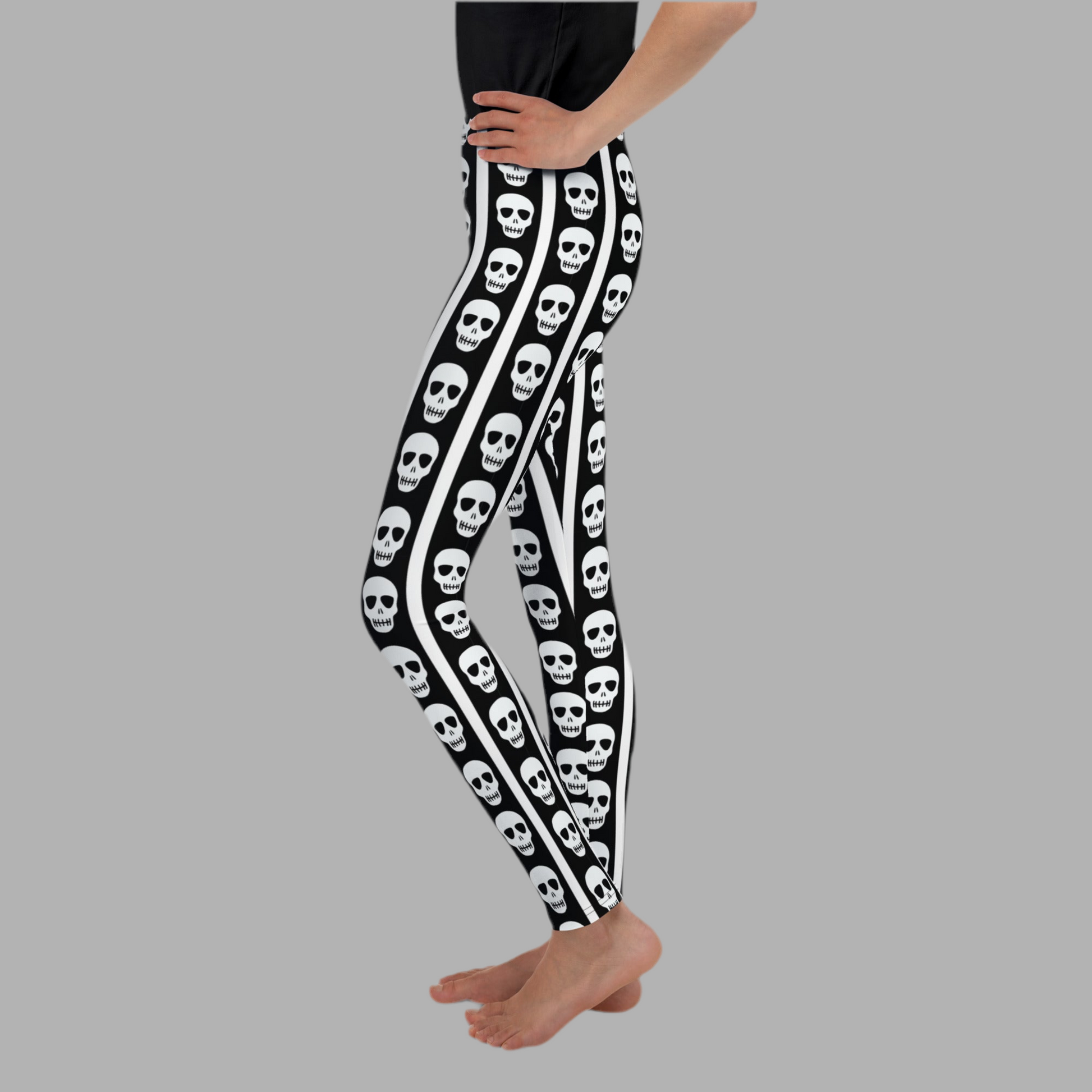 Girls and tween skull leggings with bold black background and white vertical stripes accented by repeating skull graphics. Comfortable stretchy youth leggings designed for all day wear in sizes 8 to 20. Perfect Halloween leggings for tweens, school outfits, fall festivals, and spooky season styling. Soft breathable fabric ideal for active kids who love edgy gothic inspired fashion and standout statement pieces.