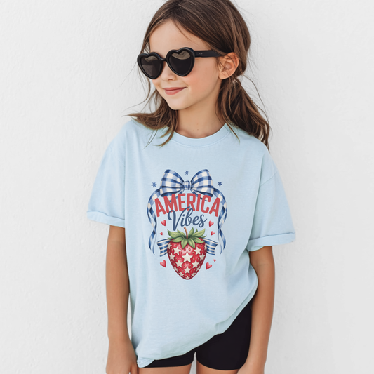 Girls patriotic strawberry Comfort Colors 9018 shirt in chambray featuring vintage Americana artwork with strawberry graphic gingham bow patriotic stars and heart accents. Soft garment dyed cotton youth tee with relaxed fit perfect for America 250 celebrations 4th of July outfits mommy and me matching looks patriotic family photos Memorial Day summer vacations and red white and blue holiday style for girls