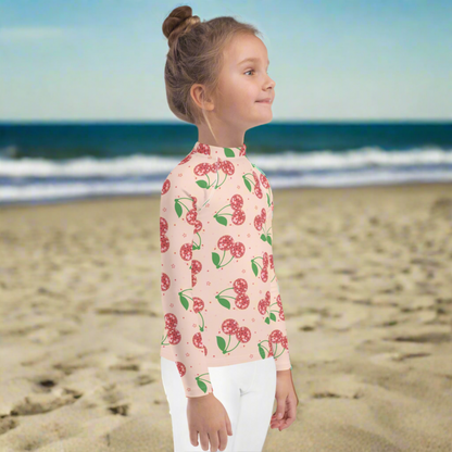 Girls pink cherry rash guard with long sleeves and a fitted design, made for toddlers sizes 2T to 7. Features a vibrant disco cherry pattern and provides UPF 50 sun protection for safe outdoor play. This swim top is perfect for beach vacations, pool days, and summer activities. Soft stretch fabric ensures comfort and flexibility. Part of a matching mommy and me swim collection for fun and coordinated family style.