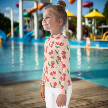 Girls swim rash guard with disco cherry print on a light pink background, available in toddler sizes 2T to 7. This long sleeve swim top provides UPF 50 sun protection and a smooth stretch fit for all day comfort. Designed for active kids, it is perfect for pool days, beach trips, splash pads, and outdoor summer fun. A playful and trendy kids swimwear piece with matching mommy and me options for family coordination.