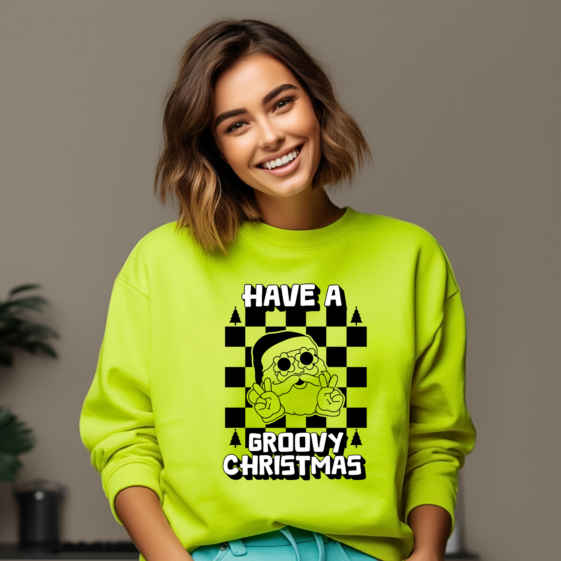 Groovy Santa Sweatshirt in Safety Pink and Safety Green, featuring a retro Santa Claus with daisy sunglasses giving a peace sign over a black checkerboard background. White block letters read “Have a Groovy Christmas,” making this vintage holiday pullover perfect for Christmas parties, retro holiday outfits, family matching sweatshirts, or a unique Christmas gift. Cozy unisex crewneck available in sizes S–5XL, ideal for spreading festive cheer with a fun retro twist.