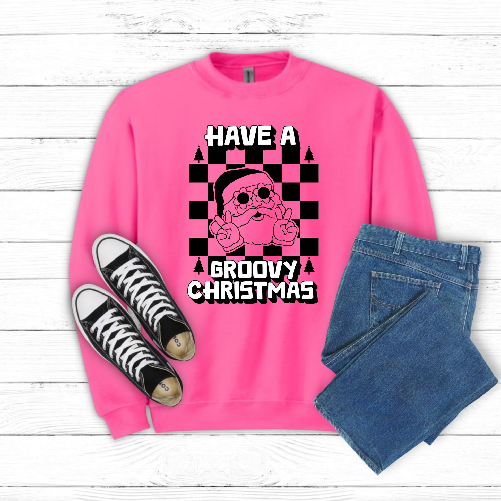 Retro Christmas sweatshirt featuring a groovy Santa Claus design with daisy sunglasses and peace sign, set against a trendy black checkerboard backdrop. This cozy Gildan 18000 crewneck is available in Safety Pink and Safety Green, making it a fun statement piece for Christmas parties, casual holiday wear, or family matching outfits. Sizes S–5XL make this festive sweatshirt a great unisex gift for anyone who loves vintage holiday style.