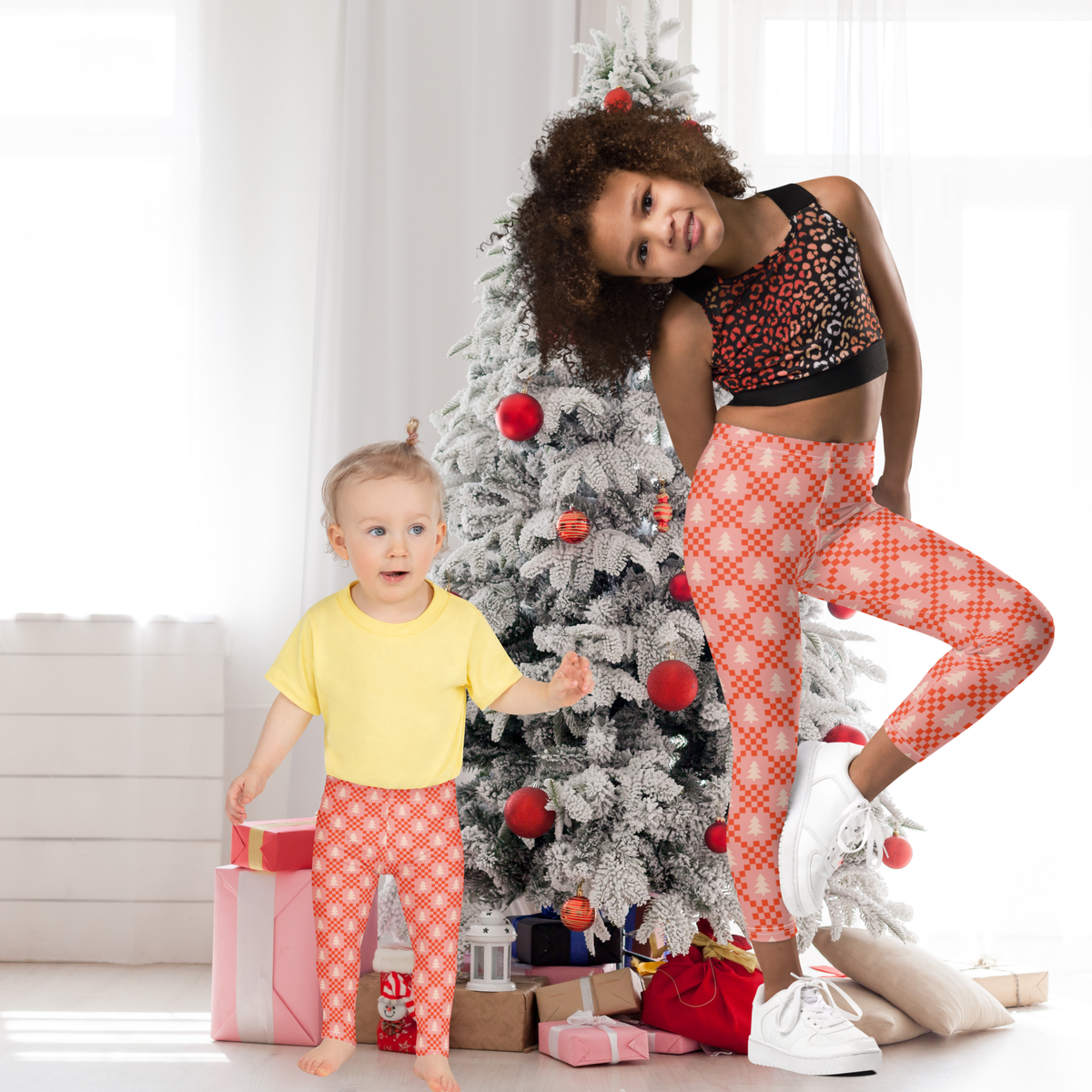 Girls wearing pink Christmas leggings with a comfortable high rise waistband and full length ankle design. The leggings feature a playful combination of soft pink, cream, and red with evergreen trees and geometric holiday details. The stretchy fabric makes them practical for active kids while the festive pattern works for Christmas morning, decorating the tree, school celebrations, family photos, or casual winter days.
