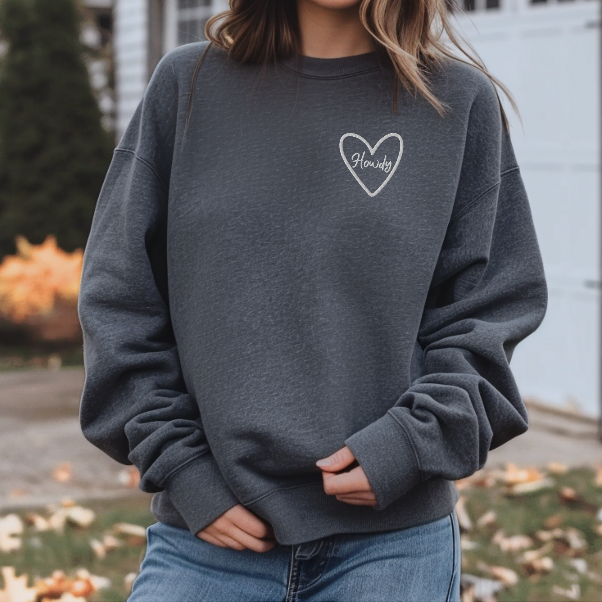 Embroidered Howdy sweatshirt made on Gildan 18000 heavy blend crewneck featuring cozy relaxed fit and soft fleece interior. Western inspired game day sweatshirt perfect for Texas college football, tailgates, and stadium events. Unisex design ideal for layering during fall sports season. Available in multiple colors including maroon, black, forest green, heliconia, and dark heather. Stylish casual outfit for students, fans, and alumni.