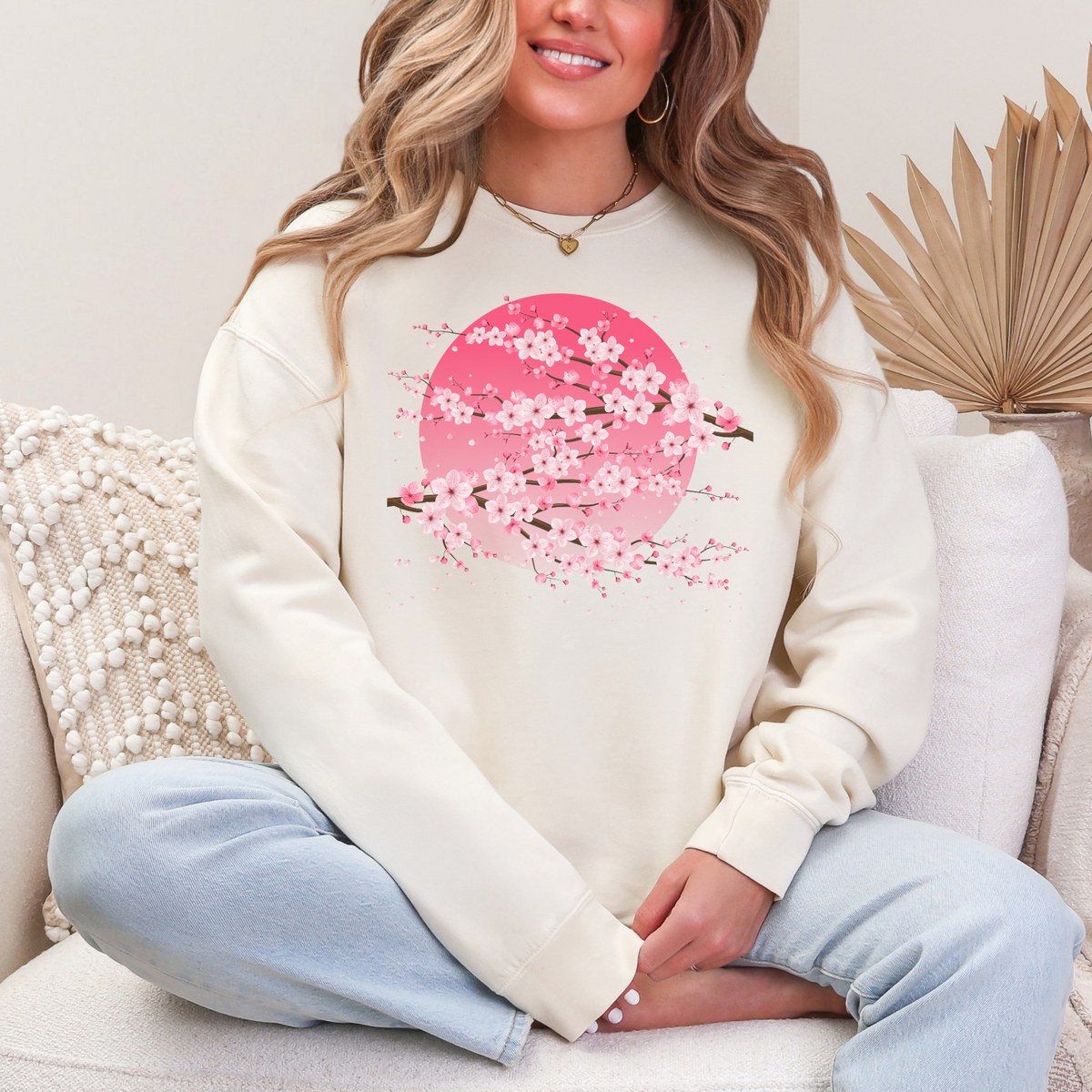 Ivory Comfort Colors 1466 pullover sweatshirt featuring delicate pink sakura cherry blossom branches arranged across a soft pink moon graphic. The neutral ivory background creates a soft feminine look that pairs easily with jeans, leggings, and casual layers, making this cozy floral sweatshirt a versatile choice for everyday wear, spring outfits, and cherry blossom lovers.