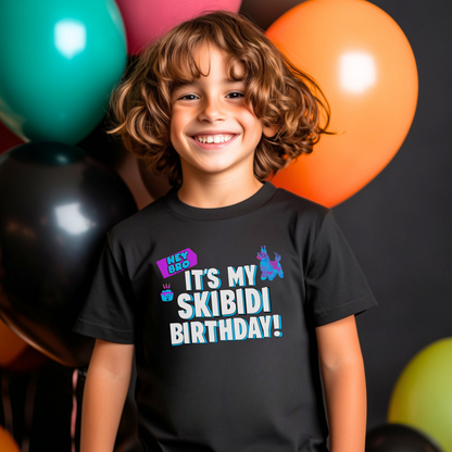 A smiling young boy with curly brown hair stands in front of colorful balloons wearing a black graphic t-shirt that reads 'IT'S MY SKIBIDI BIRTHDAY!' in white and blue letters with a purple party hat graphic. Kids Skibidi birthday shirt featuring a colorful Hey Bro It’s My Skibidi Birthday graphic with bold blue and white lettering on a black Bella Canvas youth tee, perfect for a funny birthday party outfit