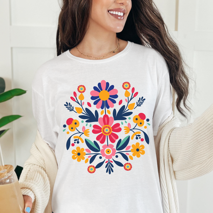 White Gildan 64000 Softstyle shirt featuring a colorful Otomi inspired floral graphic with bright Mexican folk art motifs. The vivid artwork stands out against the white cotton tee, creating a cheerful Mexican folk art shirt for everyday wear, Hispanic Heritage Month, fiestas, cultural celebrations, family photos, or anyone who enjoys colorful floral graphic tees with a distinctive folk art aesthetic.