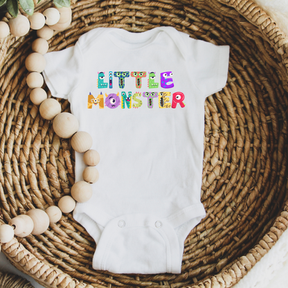 Flat lay of the white Little Monster baby bodysuit, featuring colorful cartoon monster letters spelling “little monster” across the front. Printed on a soft Bella + Canvas 100B one-piece, this breathable cotton bodysuit has an envelope neckline and three-snap leg closure for easy diaper changes. Perfect as a first Halloween outfit, fall romper, or baby shower gift, available in newborn through 24 months, and designed for everyday comfort and durability.