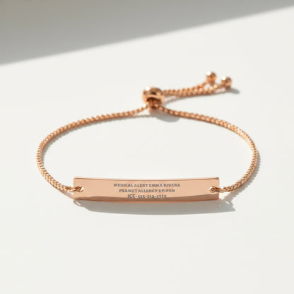 A rose gold medical alert bracelet featuring a horizontal bar engraved with personal and allergy information, suspended on a matching adjustable chain with a sliding clasp, shown on a plain white background.