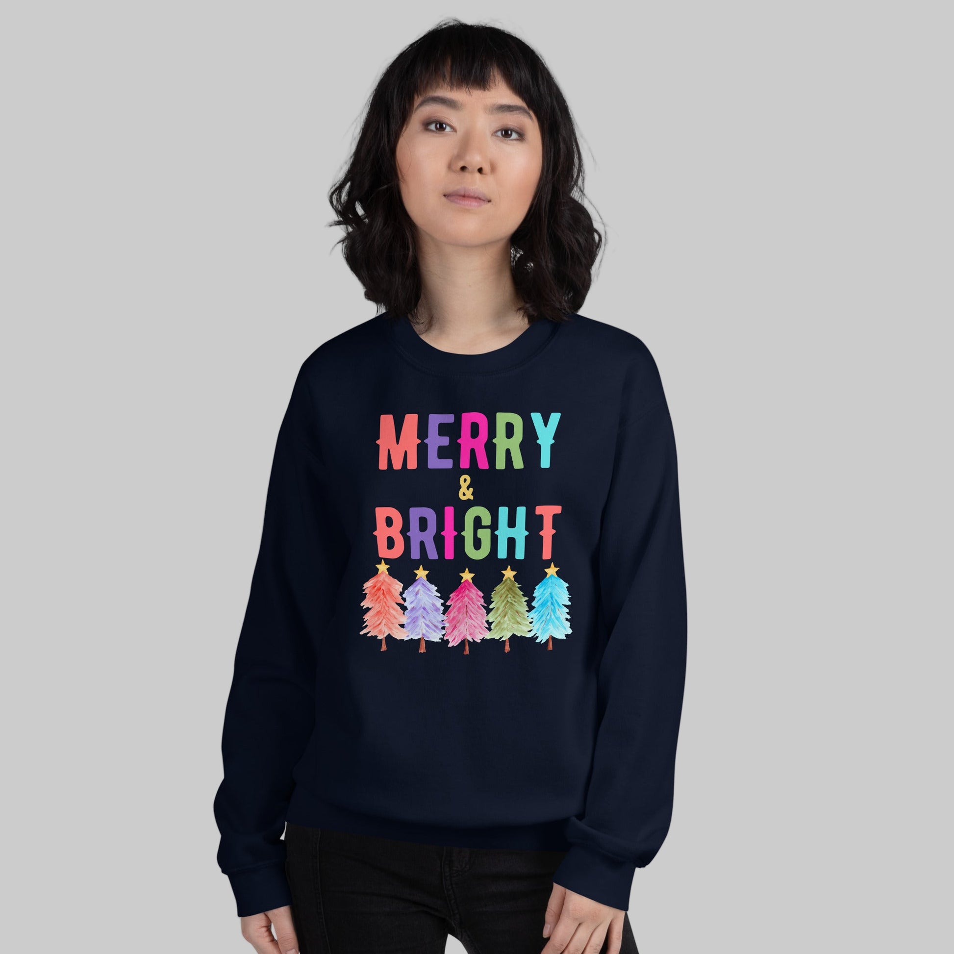 Celebrate the holidays in style with this Merry and Bright Christmas sweatshirt featuring colorful trees and merry lettering. Printed on the warm and durable Gildan 18000, this unisex sweatshirt comes in white, navy, and black with inclusive sizes S to 5XL. A perfect Christmas gift shirt for teachers, moms, or friends, this holiday sweatshirt is great for festive gatherings, casual wear, or cozy winter nights with family.