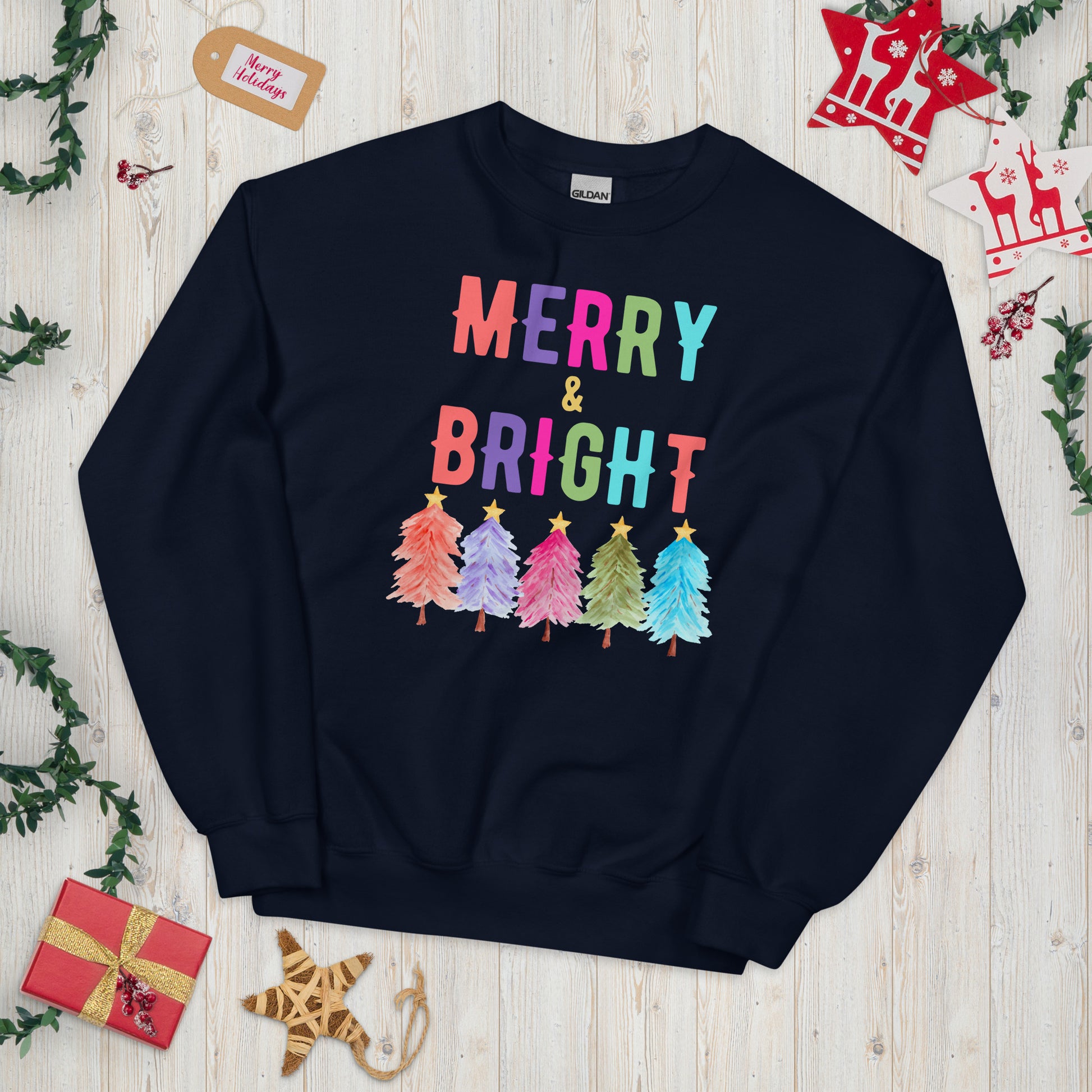 This Merry and Bright sweatshirt brings joy to your holiday wardrobe with a festive rainbow tree design on the Gildan 18000 crewneck. With a cozy interior and relaxed fit, this unisex Christmas sweatshirt is available in white, navy, and black in sizes S to 5XL. Ideal for Christmas parties, holiday photos, or everyday winter wear, this sweatshirt makes a perfect holiday gift idea for moms, teachers, friends, or family.