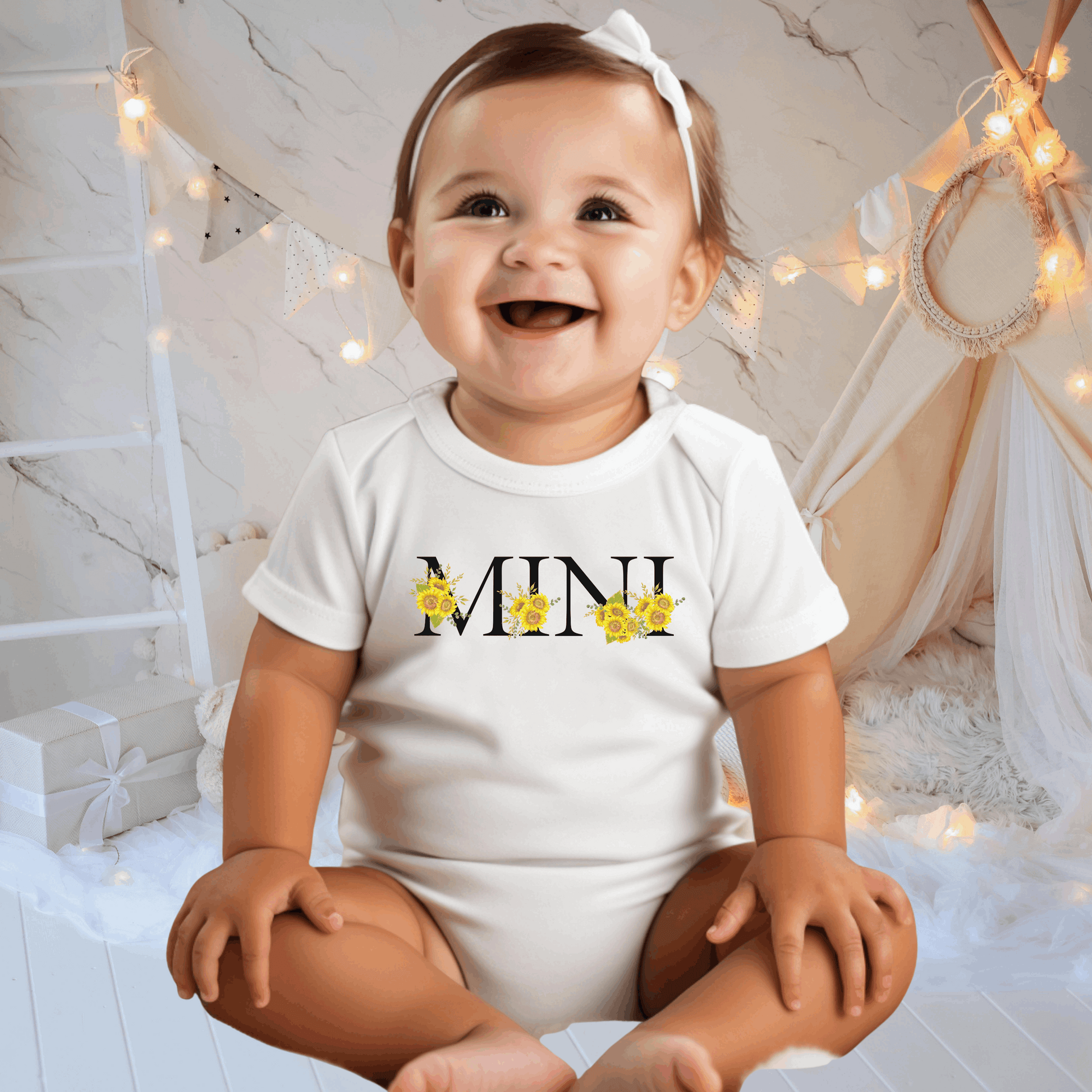 Mini Sunflower Baby Bodysuit in White or Pink, made from soft Bella Canvas 100B fabric, perfect for delicate skin. Features charming sunflower calligraphy reading “MINI” and coordinates with MAMA sweatshirt and tee for a matching family outfit. Cozy, breathable, and stylish for everyday wear, family photos, special occasions, or gifting, this baby bodysuit combines comfort, practicality, and adorable design in one wardrobe essential.