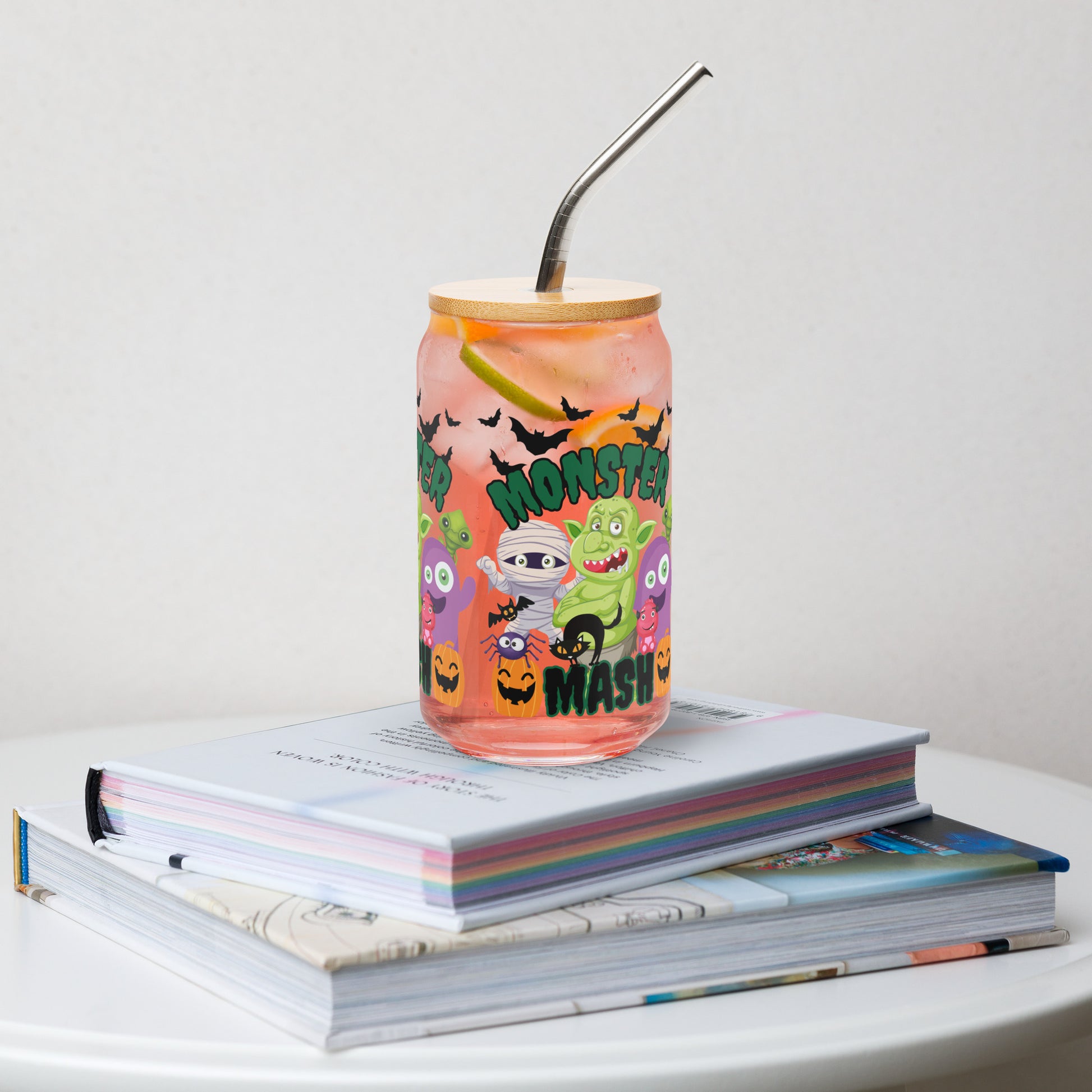 Monster Mash 16 oz reusable glass can with bamboo lid and straw, decorated with colorful monsters, bats, and pumpkins. Ideal Halloween iced coffee cup, cocktail glass, or soda tumbler for festive fall gatherings and parties. Fun spooky season drinkware for everyday sipping or entertaining. Makes a unique eco-friendly gift for friends, family, or teachers. Trendy reusable Halloween glass cup and durable fall beverage can.