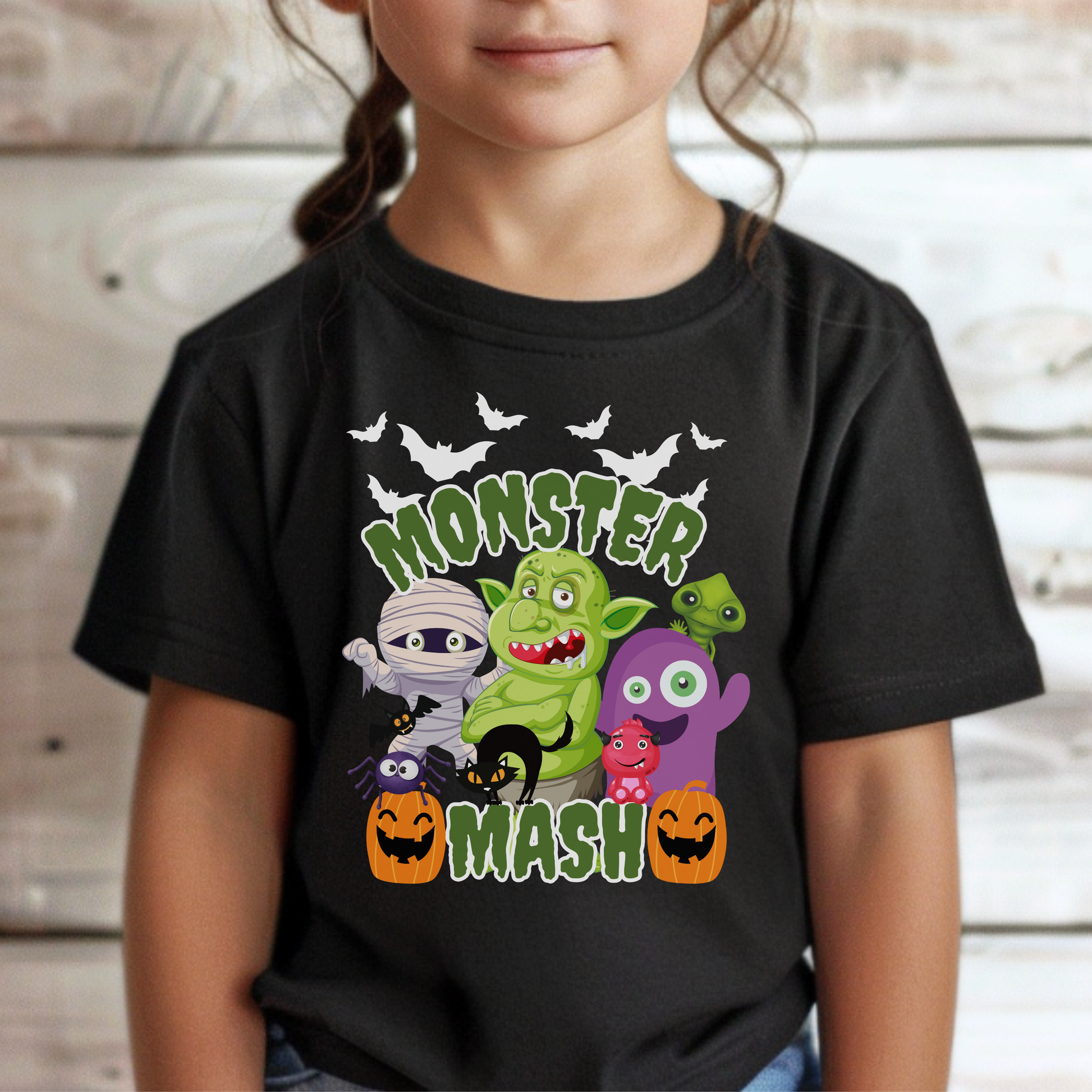 Monster Mash Halloween shirt featuring a fun cartoon style graphic with bats, zombies, trolls, mummy, ghost, black cat, and pumpkins arranged on a black Bella Canvas tee. The design includes green slime lettering that says Monster Mash, making it a playful Halloween shirt for kids and adults, perfect for pumpkin patch visits, trick or treating, school parties, and family matching Halloween outfits.
