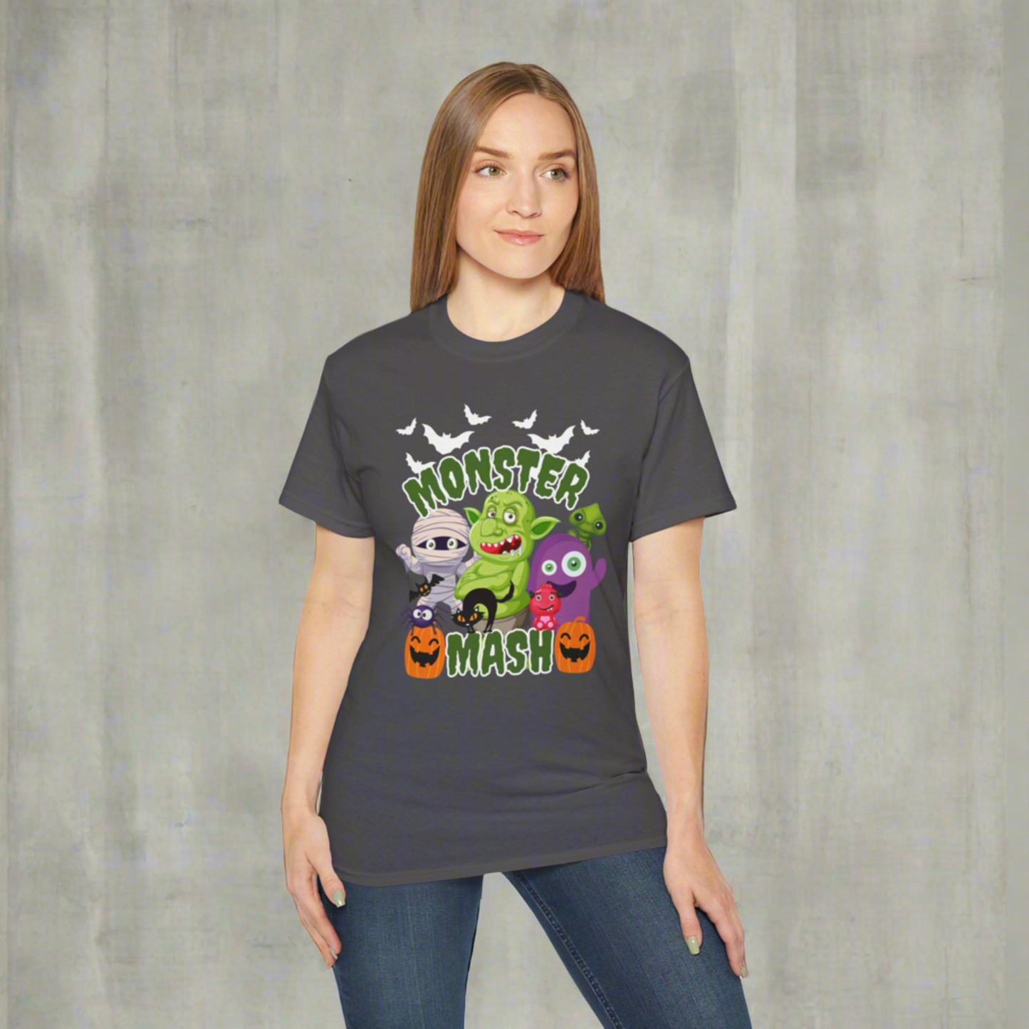 Flat lay of a Monster Mash Halloween graphic tee for adults, featuring playful cartoon designs of a mummy, pumpkins, black cat, spooky spider, bats, and a troll. Printed on a soft black or charcoal Gildan 2000 shirt, this unisex Halloween shirt is available in sizes S–5XL. Perfect for haunted houses, trick-or-treating, fall festivals, or casual spooky season outfits, this festive t-shirt makes a fun Halloween gift idea.