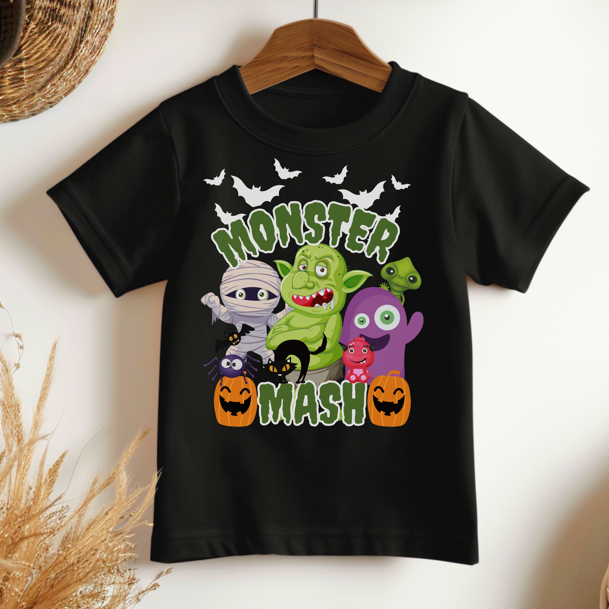 Cute Monster Mash Halloween shirt on a black Bella Canvas tee featuring playful cartoon monsters including zombies, trolls, mummy, ghost, black cat, bats, and pumpkins. The design includes bright green slime style lettering that reads Monster Mash, perfect for spooky season outfits, pumpkin patch trips, school Halloween events, trick or treating, and coordinated family matching Halloween shirts.