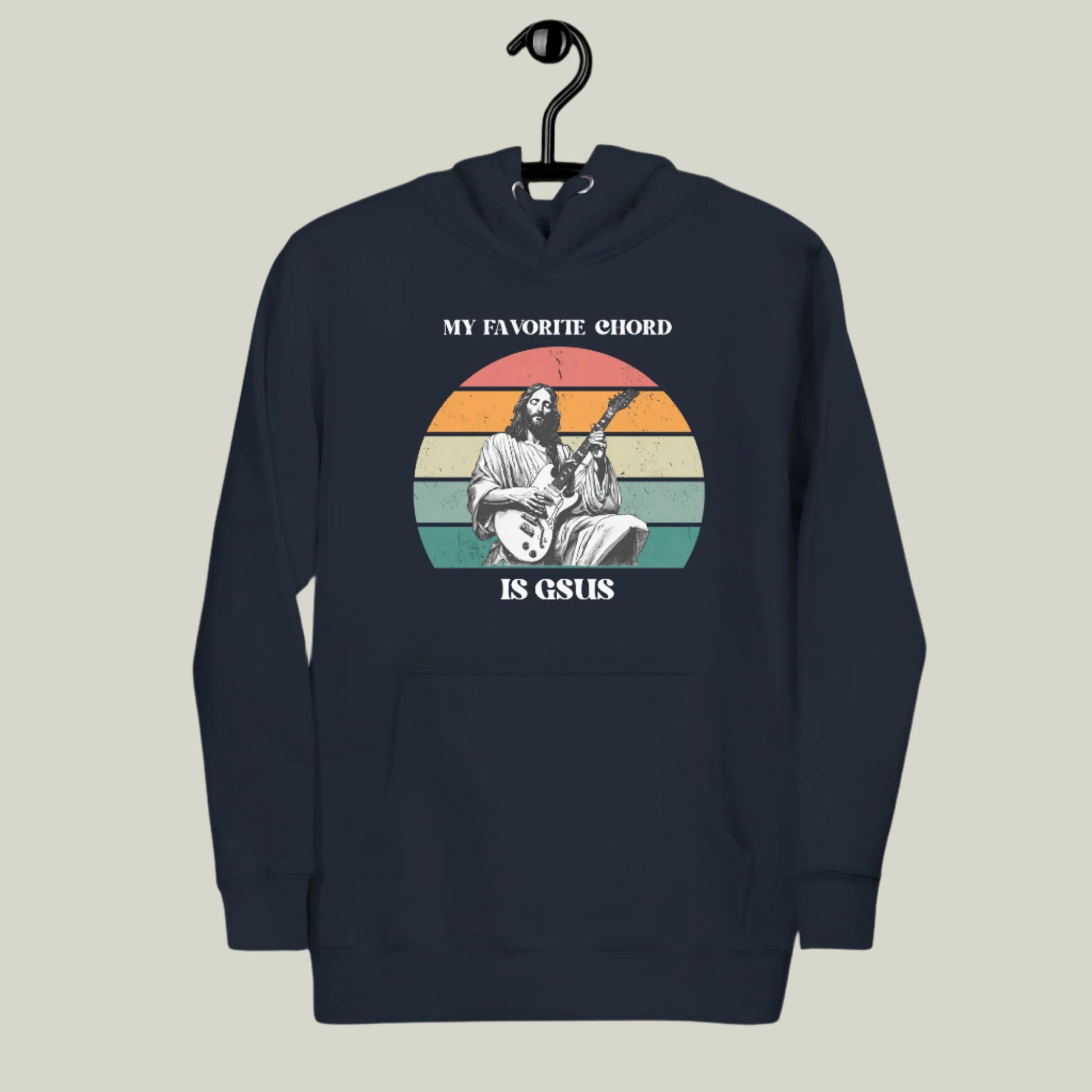 Hanging mockup of the “My Favorite Chord Is GSUS” unisex hoodie, displayed on a wooden hanger to highlight its soft fleece fabric and relaxed fit. Featuring a witty Christian pun that blends music and faith, this cozy hoodie is perfect for musicians, worship leaders, and church band members. Made from a cotton-poly blend and available in sizes S–3XL, it’s ideal for gifts or everyday wear.

