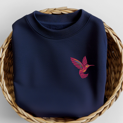 Folded navy Gildan crewneck sweatshirt featuring a colorful embroidered hummingbird design on the chest. The folded view clearly shows the deep navy fabric and detailed bird embroidery while giving shoppers a close look at the sweatshirt color and overall design. This classic crewneck is an easy everyday option for hummingbird lovers, bird lovers, gardeners, bird watchers, and anyone who enjoys nature inspired embroidered clothing.