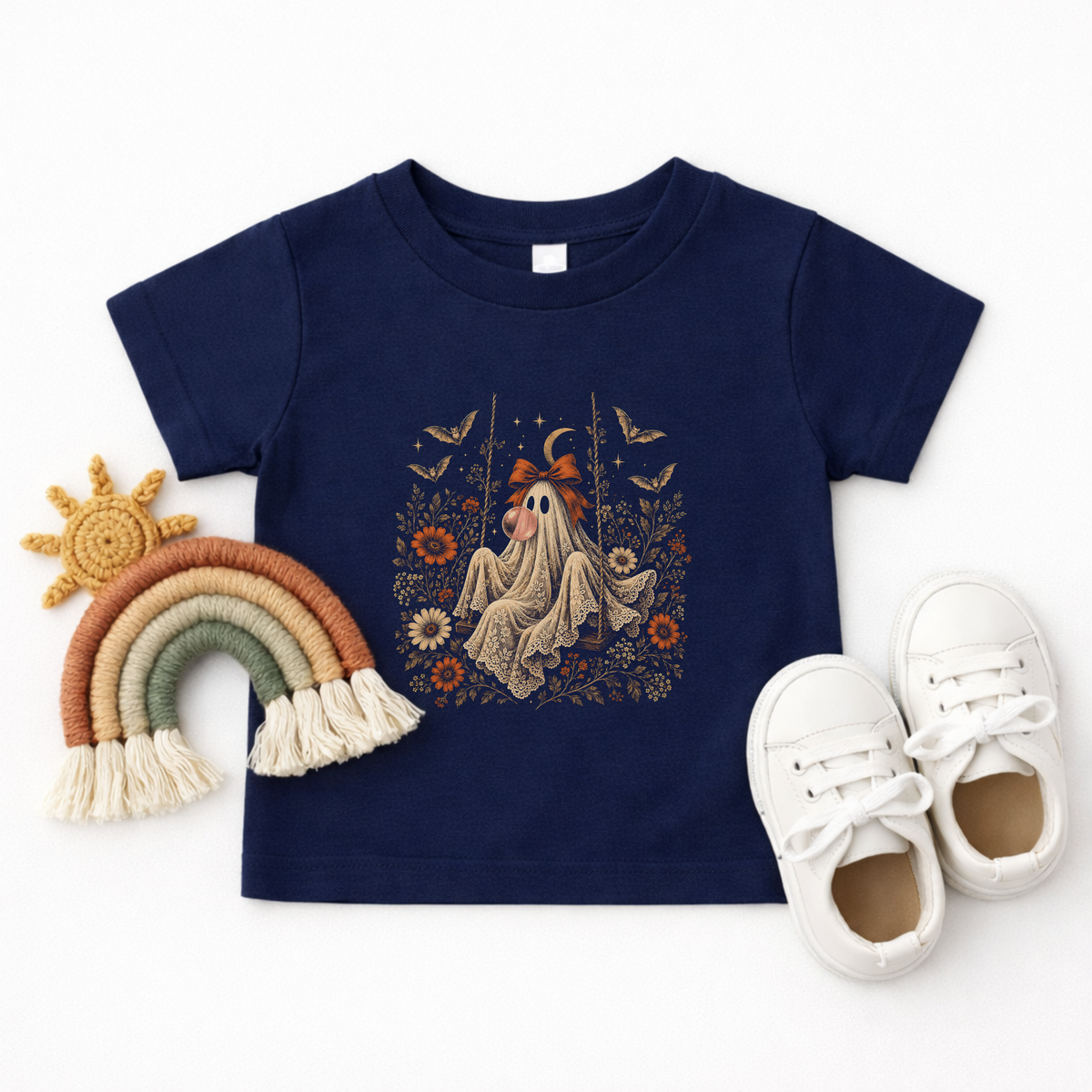Navy toddler Halloween T shirt shown in a flatlay featuring a whimsical vintage ghost blowing bubble gum, surrounded by orange flowers, botanical foliage, bats, stars, lace and a bow. A cute Halloween graphic tee for toddlers who love ghosts, fall fashion and playful spooky season designs.