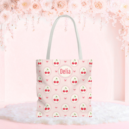 Personalized cherry tote bag with a soft pink background, repeating cherry medallions, and delicate bow accents. This custom cherry tote has a playful Cutecore and Coquette aesthetic and can be personalized with a name or monogram, making it a cute accessory for school, shopping, travel, or everyday use.