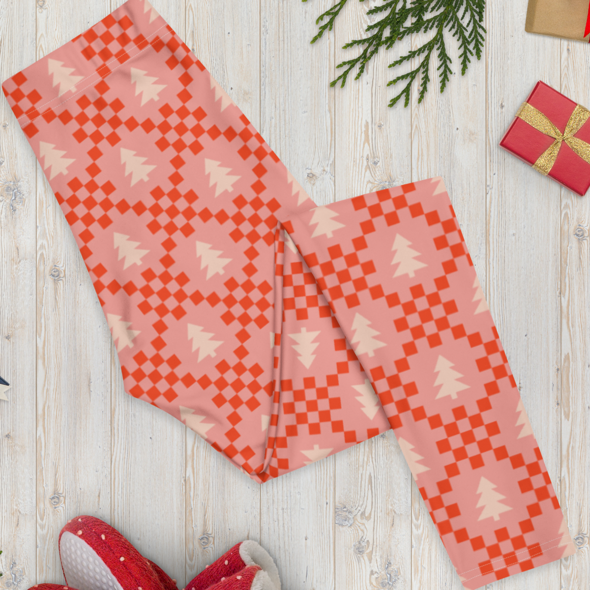 Close view of the playful print on pink Christmas tree leggings, showing cream evergreen trees surrounded by red geometric details on a soft pink background. The nostalgic pattern is inspired by retro and Nordic Christmas sweater designs while giving the traditional holiday look a fresh feminine twist. The detailed print makes these leggings easy to style with simple sweaters, sweatshirts, or holiday tees.