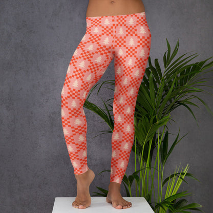Pink women's Christmas leggings featuring a repeating pattern of cream evergreen trees surrounded by red geometric shapes on a soft pink background. The playful print has a cozy Nordic inspired and nostalgic holiday feel. These full length leggings have a comfortable mid rise waistband and stretchy fabric, making them easy to wear for Christmas gatherings, holiday outings, lounging, or everyday seasonal outfits.