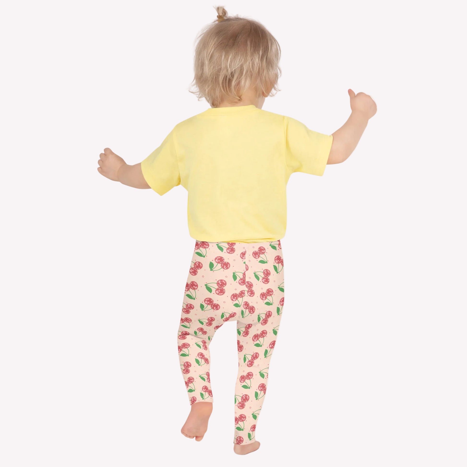 Cherry print girls leggings featuring a soft pink background with scattered red cherries and green stems, designed with a high rise waistband and full length fit. These kids leggings offer soft stretch fabric for comfort and flexibility, making them ideal for school outfits, dance practice, gymnastics, or everyday play. A playful fruit pattern design that combines cute style with durable activewear for girls who love fun, colorful fashion.