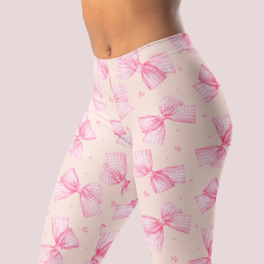 Pink Bow Coquette Leggings for Women featuring a soft pink background with delicate bow print details and a flattering mid rise waistband. Full length yoga pants made with smooth stretch polyester spandex fabric for comfortable everyday wear. Cute coquette leggings perfect as tights, workout pants, lounge pants, travel outfits, pilates wear, feminine athleisure, beach swim pants cover up styling, mommy and me matching looks, and trendy boutique fashion in sizes XS through XL.