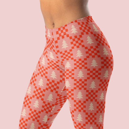 A close view of pink, red, and cream Christmas leggings showing the repeating tree and geometric pattern across the fabric. The soft pink background gives this holiday design a feminine and playful look, while the red details add a festive pop of color. These women's leggings are a fun alternative to traditional red and green Christmas clothing and can be styled throughout the holiday season.