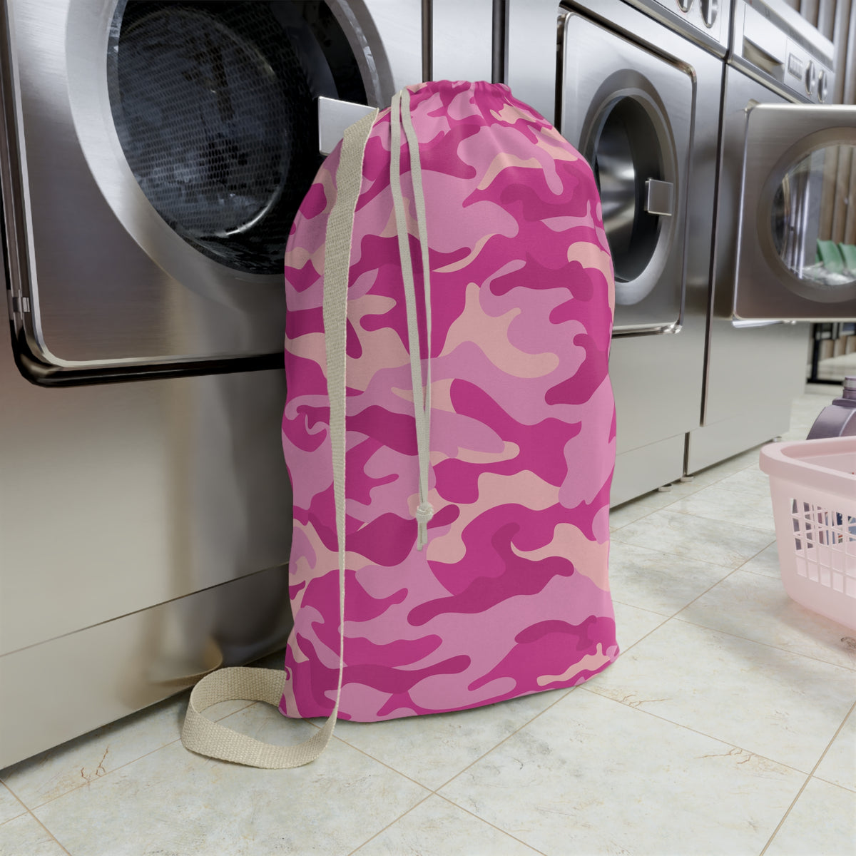 Pink camouflage laundry bag in front of a washing machine in a laundry room.