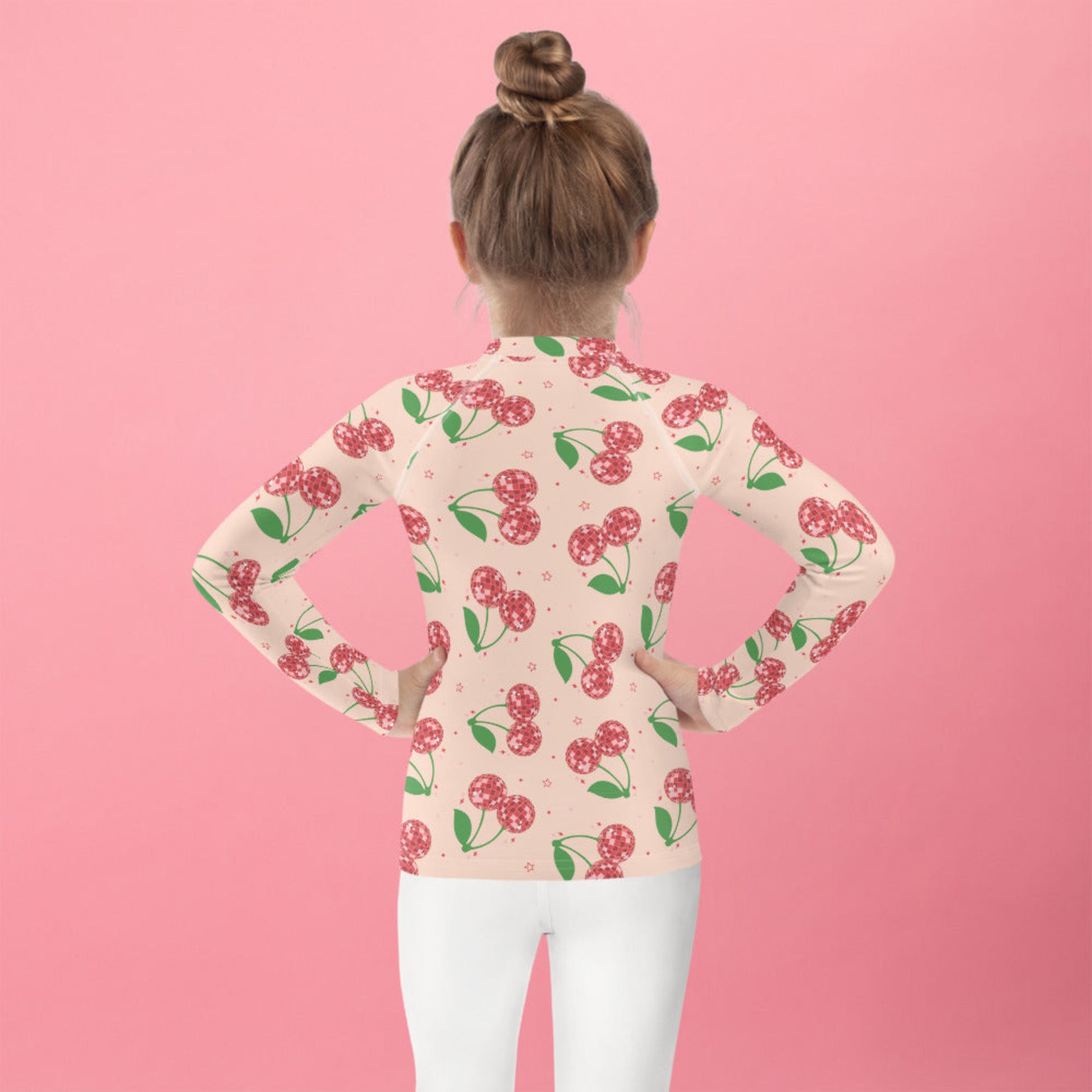 Pink cherry print girls rash guard with long sleeves and a fitted design, available in sizes 2T to 7. Features a playful disco cherry pattern on a soft pink base. Designed with UPF 50 protection to keep kids safe during outdoor play. Ideal for swimming, beach days, pool time, and summer vacations. Soft stretch fabric allows easy movement, and matching family swim options make it perfect for mommy and me outfits and coordinated vacation looks.
