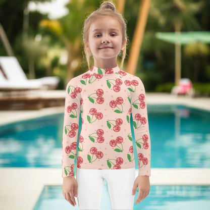 Pink disco cherry girls rash guard in sizes 2T to 7 designed with long sleeves and a fitted silhouette for sun protection and comfort. Features a fun cherry print on a soft pink background. This kids swim top offers UPF 50 protection and stretchy fabric for easy movement. Perfect for beach days, pool play, swim lessons, and summer vacations. Also available in matching mommy and me styles for coordinated family swim outfits.